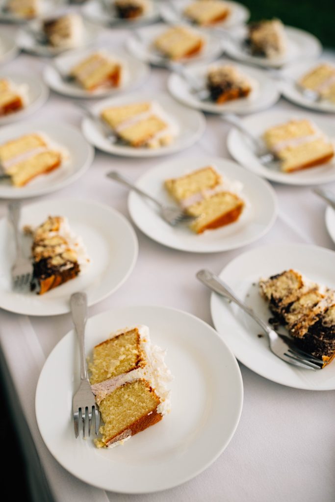 An assortment of plates on a white table each with a slice of cake and a fork on them.