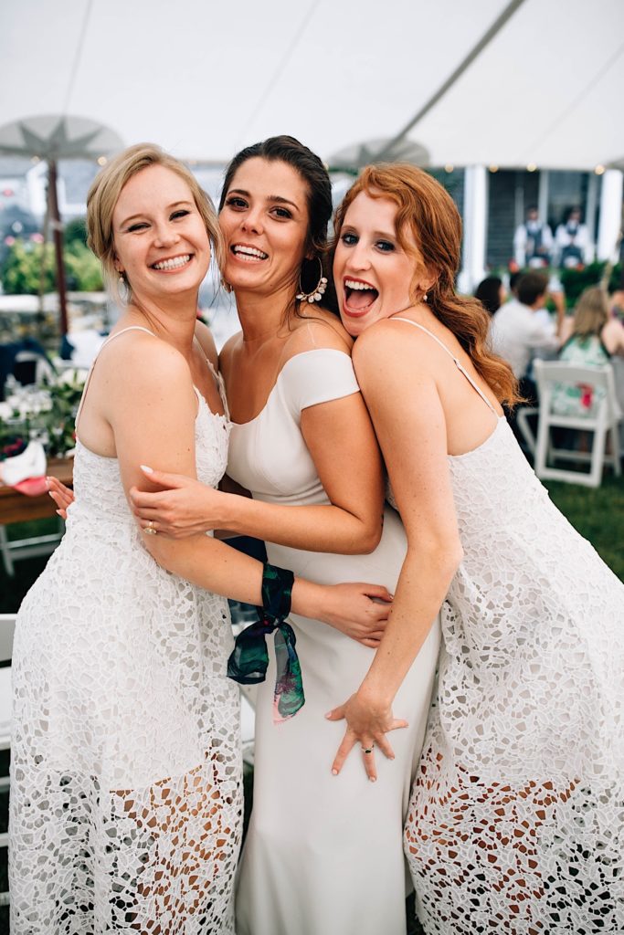 A bride stands between two of her bridesmaids as they all pose and smile at the camera together during the wedding reception.