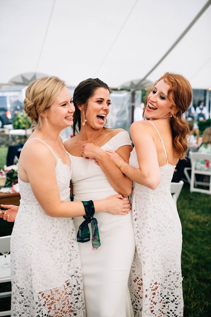 A bride stands between two of her bridesmaids as they all pose and smile at the camera together during the wedding reception.