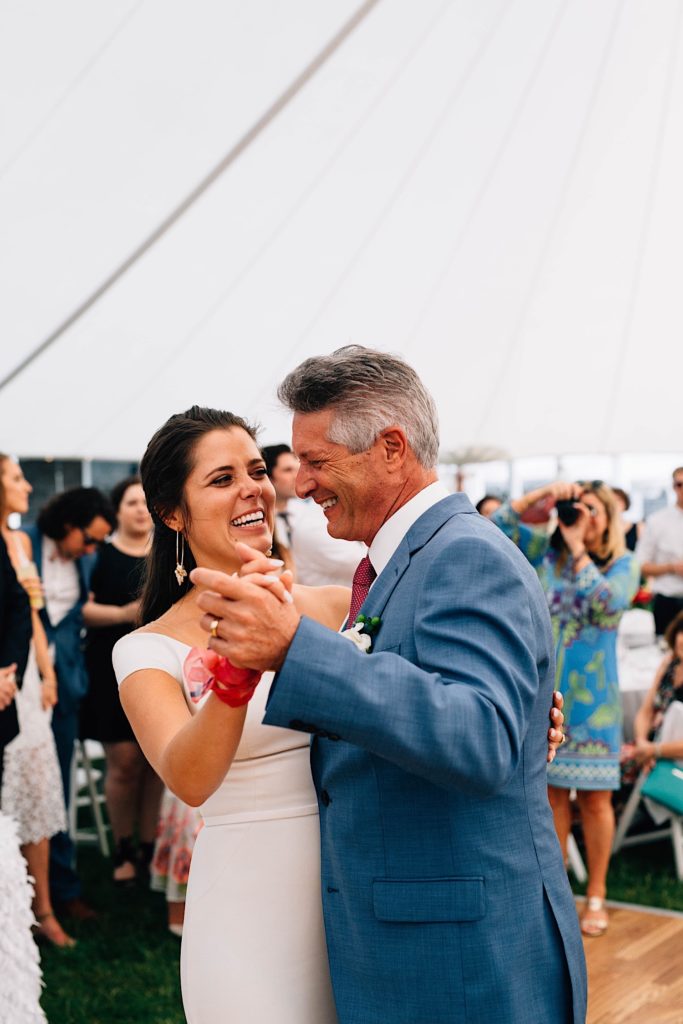 A bride and her father dance together and smile during a wedding reception.