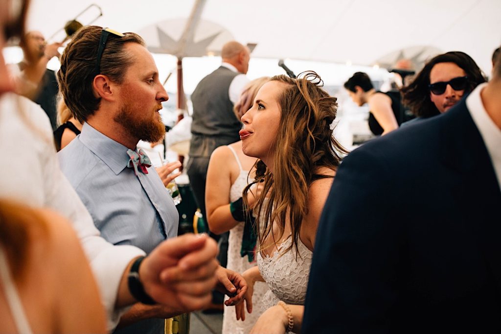 At a wedding reception a bridesmaid sticks her tongue out at a man as he looks at her.