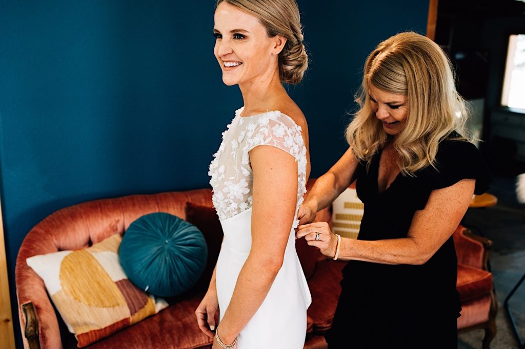 The Brides mother helps her button up her elegant low back gown on her wedding day.