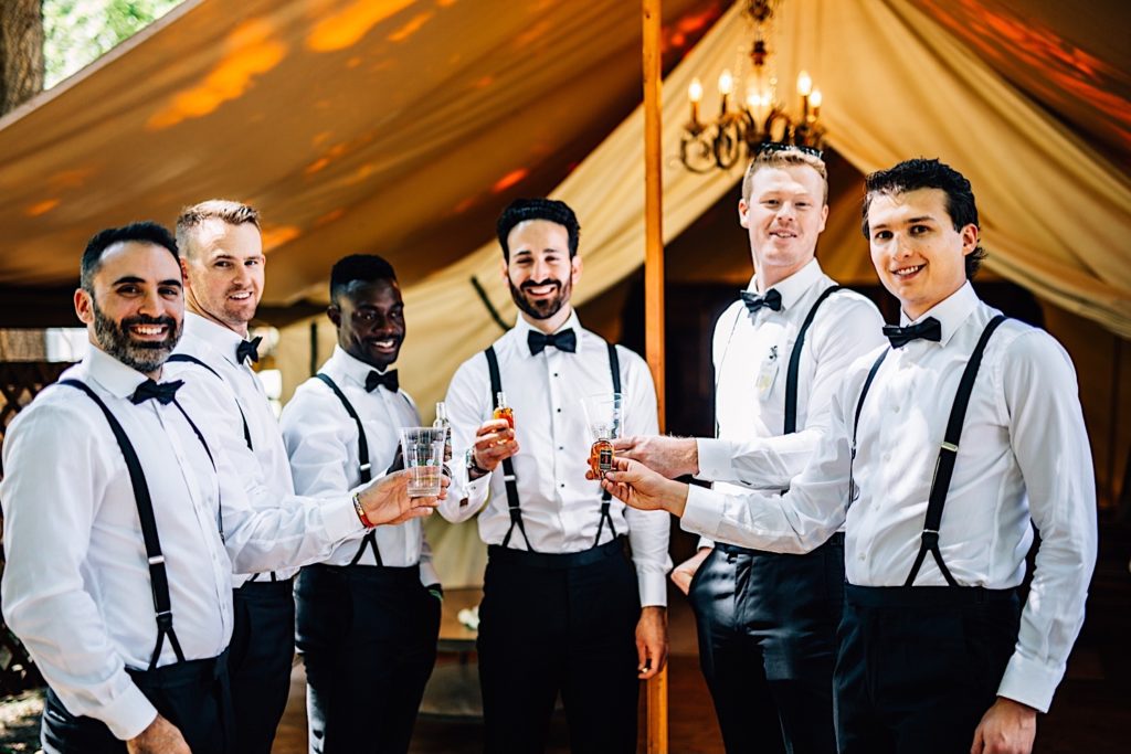 Groom and groomsmen all smile and look at the camera while doing a toast