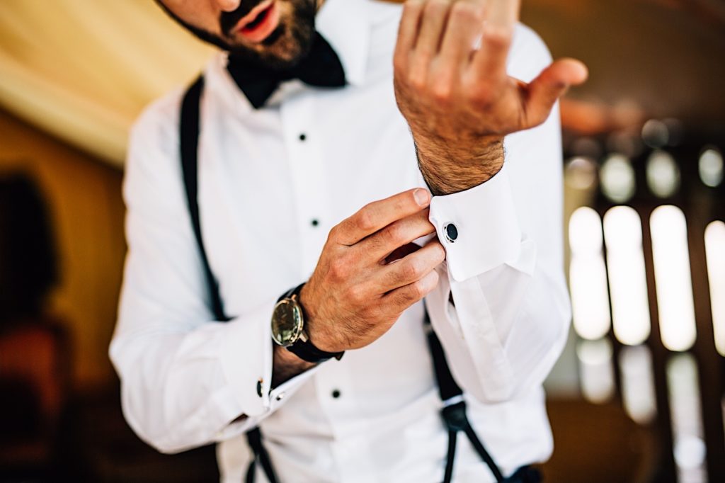 Groom adjusts his cuff links while getting ready for his wedding