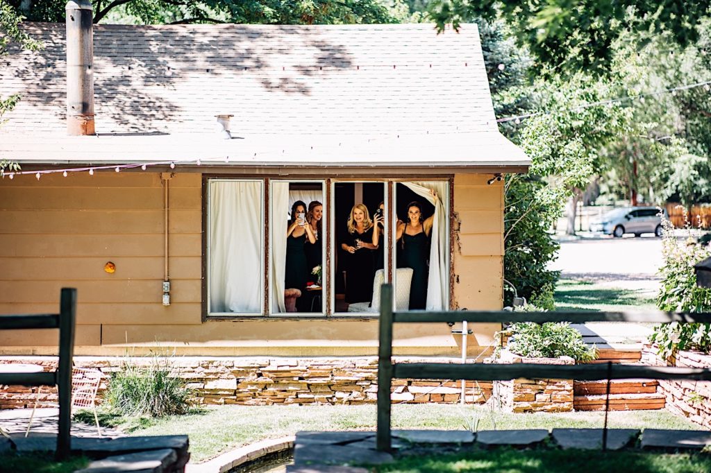 Bridesmaids and mother of the bride look out the window of the getting ready space at River Bend Colorado