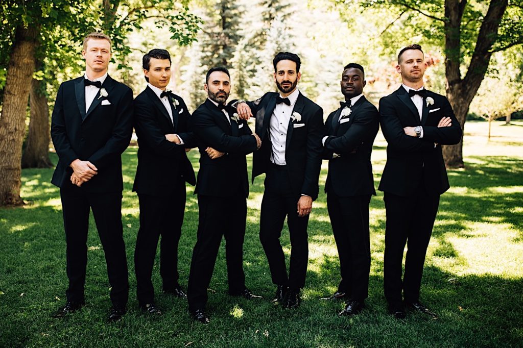Groomsmen stand together for a photo wearing all black suits with white boutonniere 