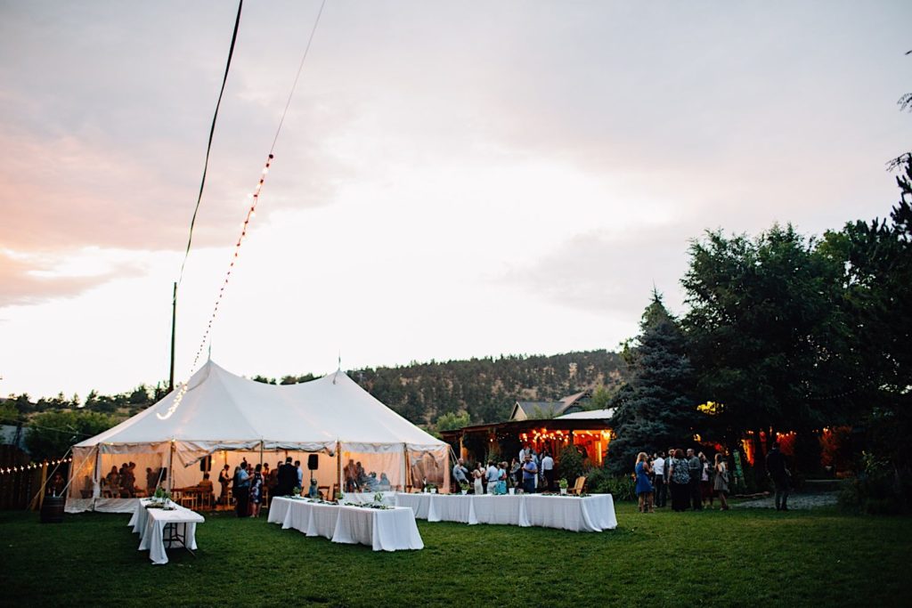 The Reception tent at Lyons Farmette in Colorado.  You can see a hill covered in trees in the background and guests around the tent.