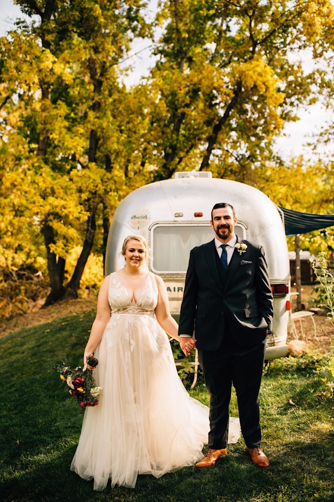 A bride and groom stand in front of the vintage airstream at Lyons Farmette, it is used as a getting ready space.