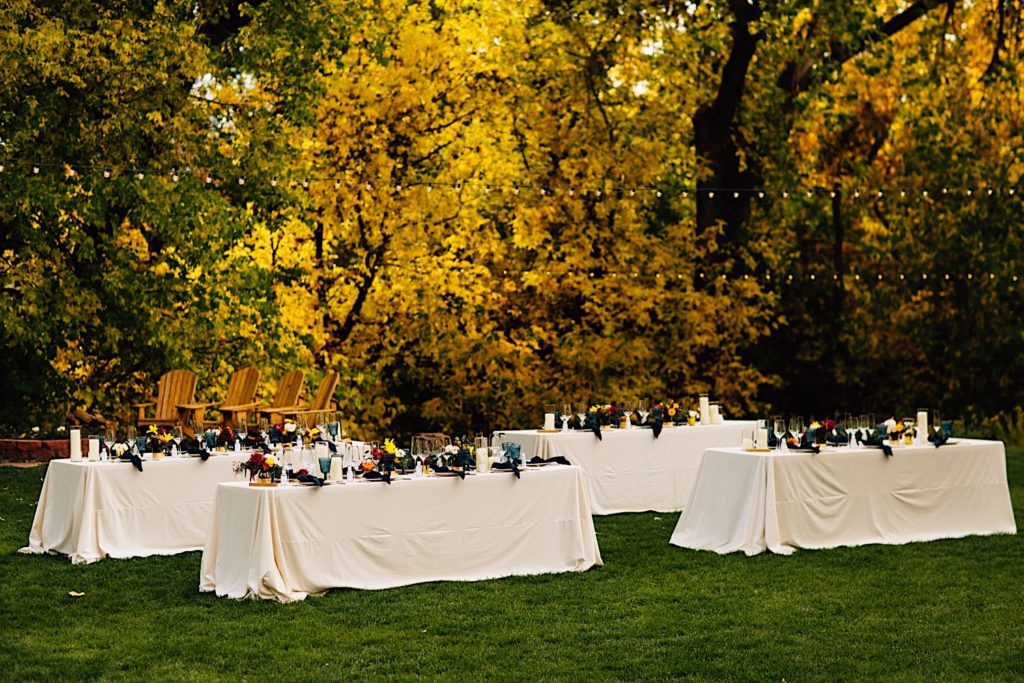 Tables are set for a wedding reception out on a lawn at Lyons Farmette in Colorado.  There are string lights hanging above.